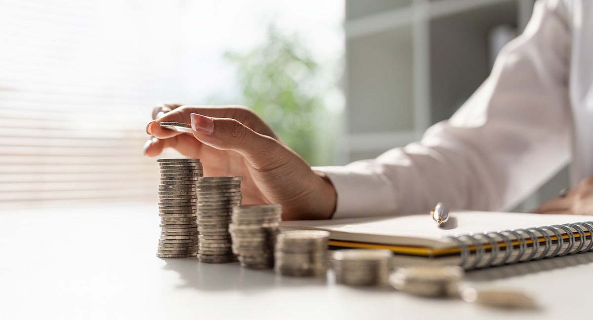 a person counting stacked quarters with a pen and pad of paper